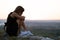 Young depressed woman in black short summer dress sitting on a rock thinking outdoors at sunset. Fashionable female contemplating