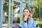 Young digital nomad, woman with tablet, working outdoors on fresh air, smiling and looking away at passerby