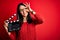 Young director woman with blue eyes making movie holding clapboard over red background with happy face smiling doing ok sign with