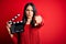 Young director woman with blue eyes making movie holding clapboard over red background pointing with finger to the camera and to