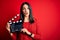 Young director woman with blue eyes making movie holding clapboard over red background scared in shock with a surprise face,