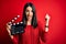 Young director woman with blue eyes making movie holding clapboard over red background screaming proud and celebrating victory and