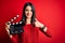 Young director woman with blue eyes making movie holding clapboard over red background with surprise face pointing finger to