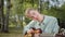 A young disabled blonde man is sitting on the plaid in the public park and playing guitar professionally