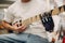 Young disabled man with artificial prosthetic hand plays on guitar at shop.