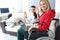 Young disabled woman in wheelchair with helper is sitting by laptop screen and waving hello