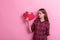 Young disgruntled girl, holds a big puzzle and looks at it. On a pink background.