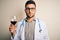 Young doctor man wearing stethoscope drinking a glass of fresh wine over isolated background with a confident expression on smart
