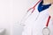 Young doctor in a medical coat, gloves and mask holds in hand a red stethoscope, listens to a patient with covid-19, coronavirus