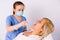 Young doctor in a medical mask and latex gloves treats the throat of an older woman with nebulizer on a white background