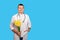 A young doctor men holds a bouquet of yellow narcissists and looks at the camera and stands on a blue background. Concept is