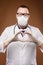 A young doctor in a protective mask and a white coat and glasses with a stethoscope around his neck shows the heart