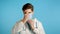 Young doctor puts on face medical mask during coronavirus pandemic. Medical stuff portrait on blue background