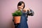 Young down syndrome gardener woman wearing worker apron holding green plant pot very happy pointing with hand and finger