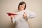 Young down syndrome woman having fun with paper plane as dream of travel happy with big smile doing ok sign, thumb up with