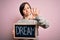 Young down syndrome woman holding blackboard with dream word as message of happiness with open hand doing stop sign with serious