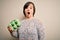 Young down syndrome woman holding cardboard egg cup from fresh healthy eggs scared in shock with a surprise face, afraid and
