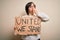 Young down syndrome woman holding protest banner with united we stand rights message cover mouth with hand shocked with shame for