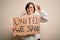 Young down syndrome woman holding protest banner with united we stand rights message doing ok sign with fingers, excellent symbol