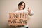 Young down syndrome woman holding protest banner with united we stand rights message happy with big smile doing ok sign, thumb up