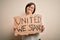 Young down syndrome woman holding protest banner with united we stand rights message with a happy face standing and smiling with a