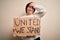 Young down syndrome woman holding protest banner with united we stand rights message stressed with hand on head, shocked with