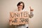 Young down syndrome woman holding protest banner with united we stand rights message surprised with an idea or question pointing