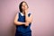 Young down syndrome woman wearing elegant shirt over pink background with hand on chin thinking about question, pensive expression