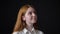 Young dreamy woman with ginger hair looking around and smiling, isolated on black background