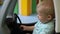 Young driver. Child closes the door in a toy car and controls the steering wheel. Baby boy, one year old. Side view.