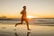 Young dynamic athlete runner man with fit strong body training on Summer sunset beach running barefoot in sport healthy and fitne