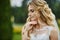 Young elegant blonde bride with closed eyes and with stylish wedding hairstyle in lace white dress outdoors