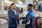 Young elegant businessman in suit and eyeglasses shaking hand of African worker of industrial plant