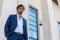 Young elegant man dressed outdoors. White marble building on the background. White shirt and jacket. Trendy hair