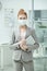 Young elegant office manager in suit and protective mask holding tablet by chest