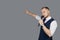 Young elegant talking man holding microphone talking with pointing finger. Isolated on grey background. Showman concept