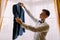 Young ellegant looking man holding out his jacket in a hotel room, preparing to dressing for an event