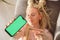 Young emotional blond woman shows smartphone with green copy space screen, focus on screen