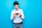 Young emotional nervous man play games by mobile phone isolated over blue wall background