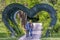 Young engaged couple walk under a green heart-shaped arch in the public park, Craiova, Romania