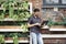 Young entrepreneur working outside using modern laptop. Standing near brick wall, plants, eco office. Successful business people