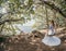 Young European beautiful girl in white bridal marriage dress posing on swing in forest trees on the ocean sea beach