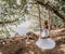 Young European beautiful girl in white bridal marriage dress posing on swing in forest trees on the ocean sea beach