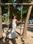 Young European beautiful girl in white bridal marriage dress standing on swing in tropical coconut palm trees forest on the ocean