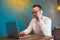 A young European businessman with glasses and a white shirt works in a laptop sitting at a table in a cafe