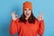 Young European excited female wearing orange sweater and cap looking at camera with opened mouth and showing ok signs with both