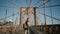 Young European female tourist with backpack walking along Brooklyn Bridge, New York and looking at smartphone 4K.