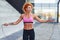 Young european redhead woman in sportive clothes jumping with rope outdoors