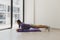 Young European woman in purple hoodie and khaki shorts doing a plank exercise at yoga mat