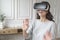 Young excited woman wearing VR headset interacting with augmented world, playing games at home